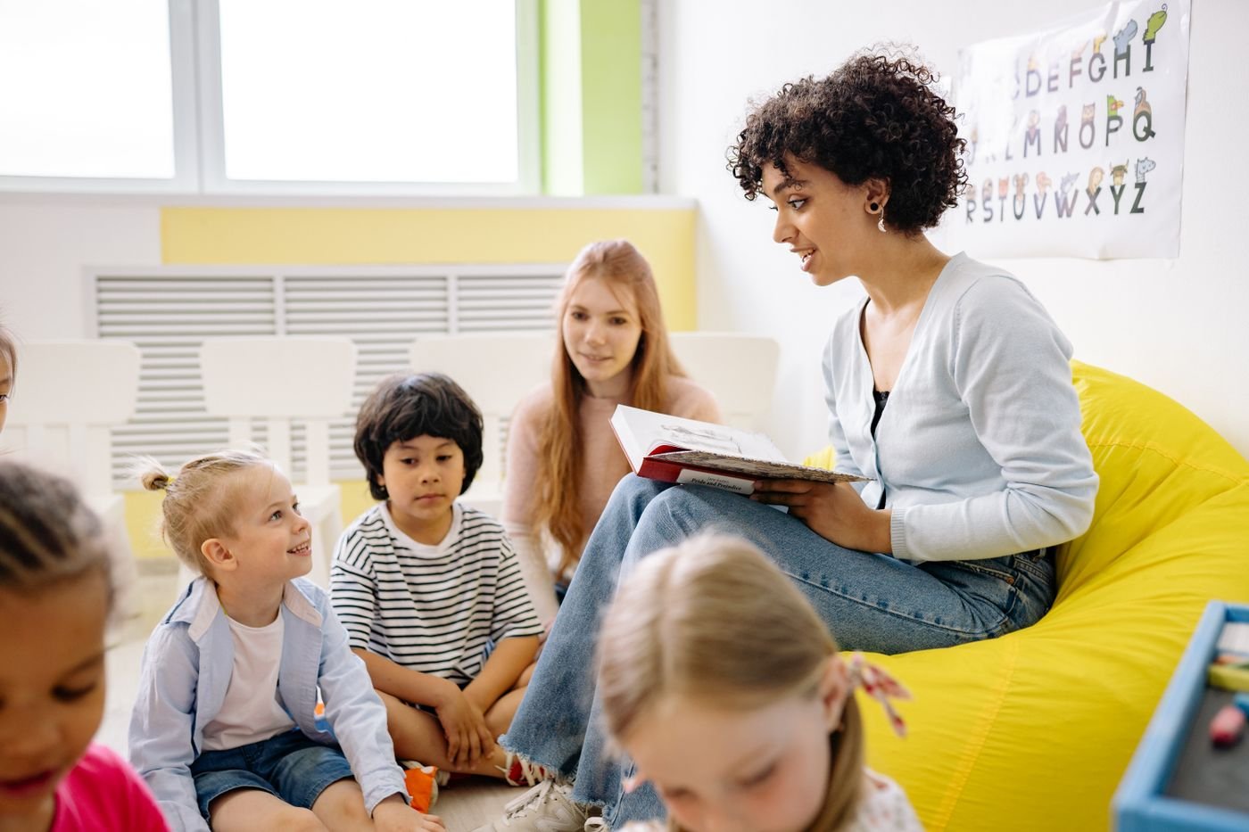 A teacher reading a picture book to a group of children sitting together on the classroom floor
