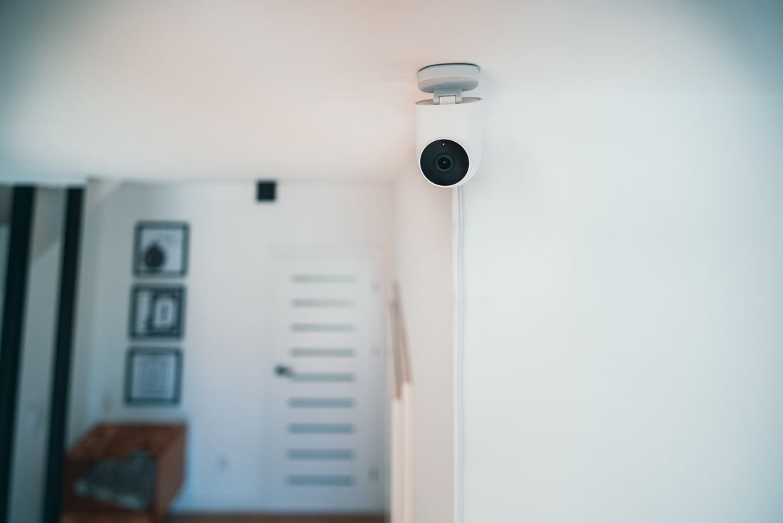A small white security camera mounted on the ceiling of a bright, calm room