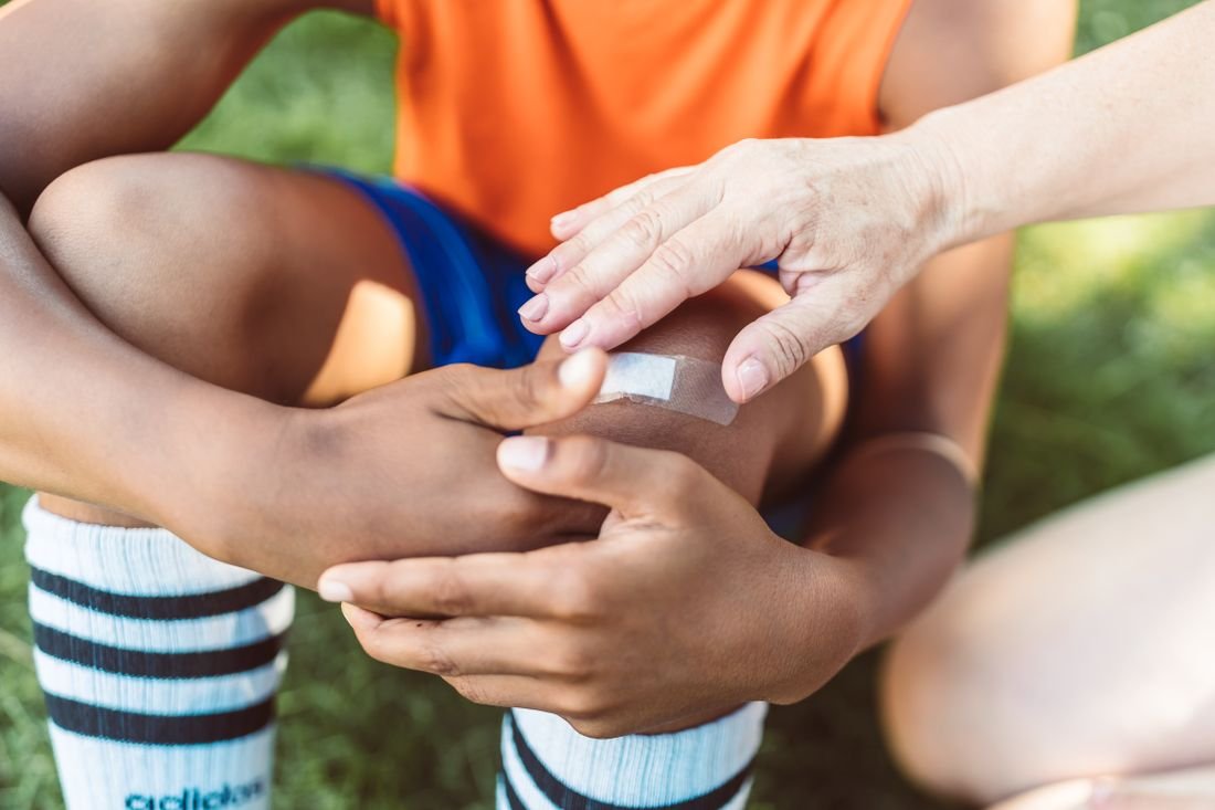 An adult carefully placing a plaster on a child’s knee