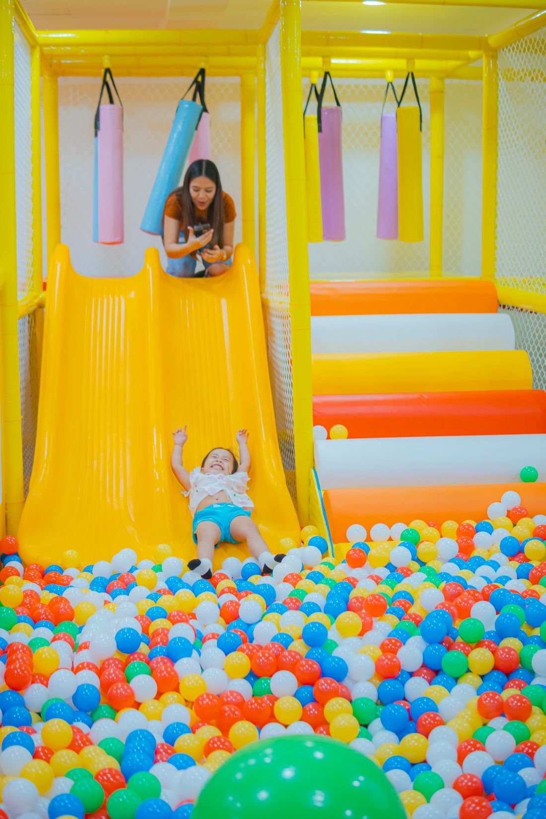 A young child sliding down into a soft ball pit in an indoor play area