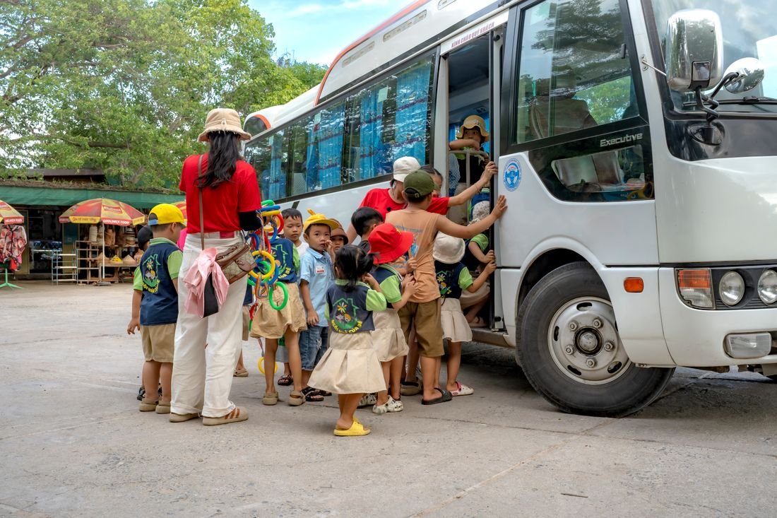A staff member supervising a group of young children as they board a school bus