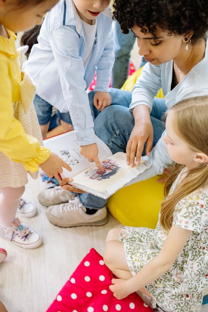 Children gathered around a teacher, looking at a picture book together