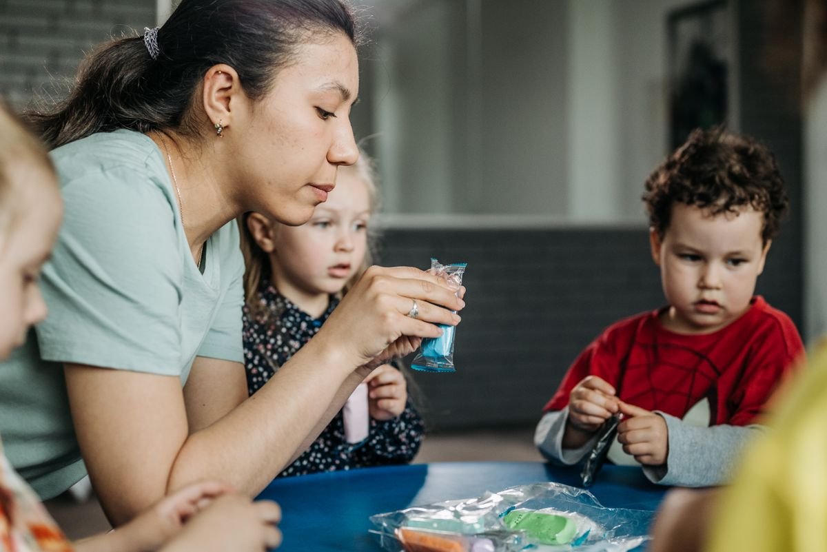 A teacher sitting with children at a table during a craft activity