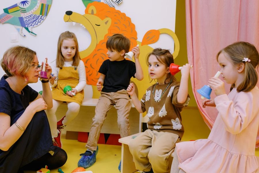 A teacher and four children playing coloured hand bells together in a nursery room