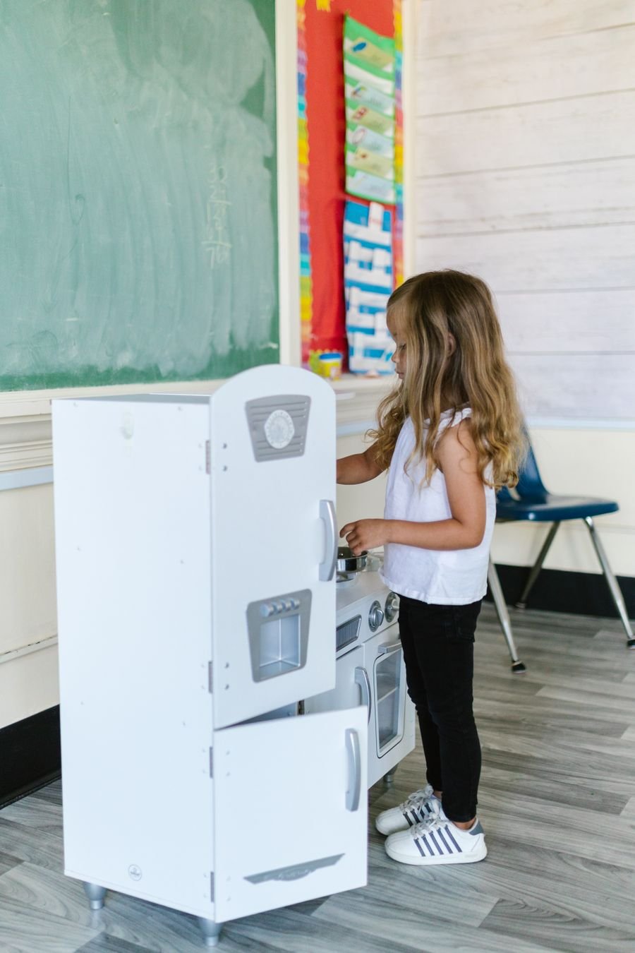 A young girl playing at a toy kitchen in a classroom role-play corner