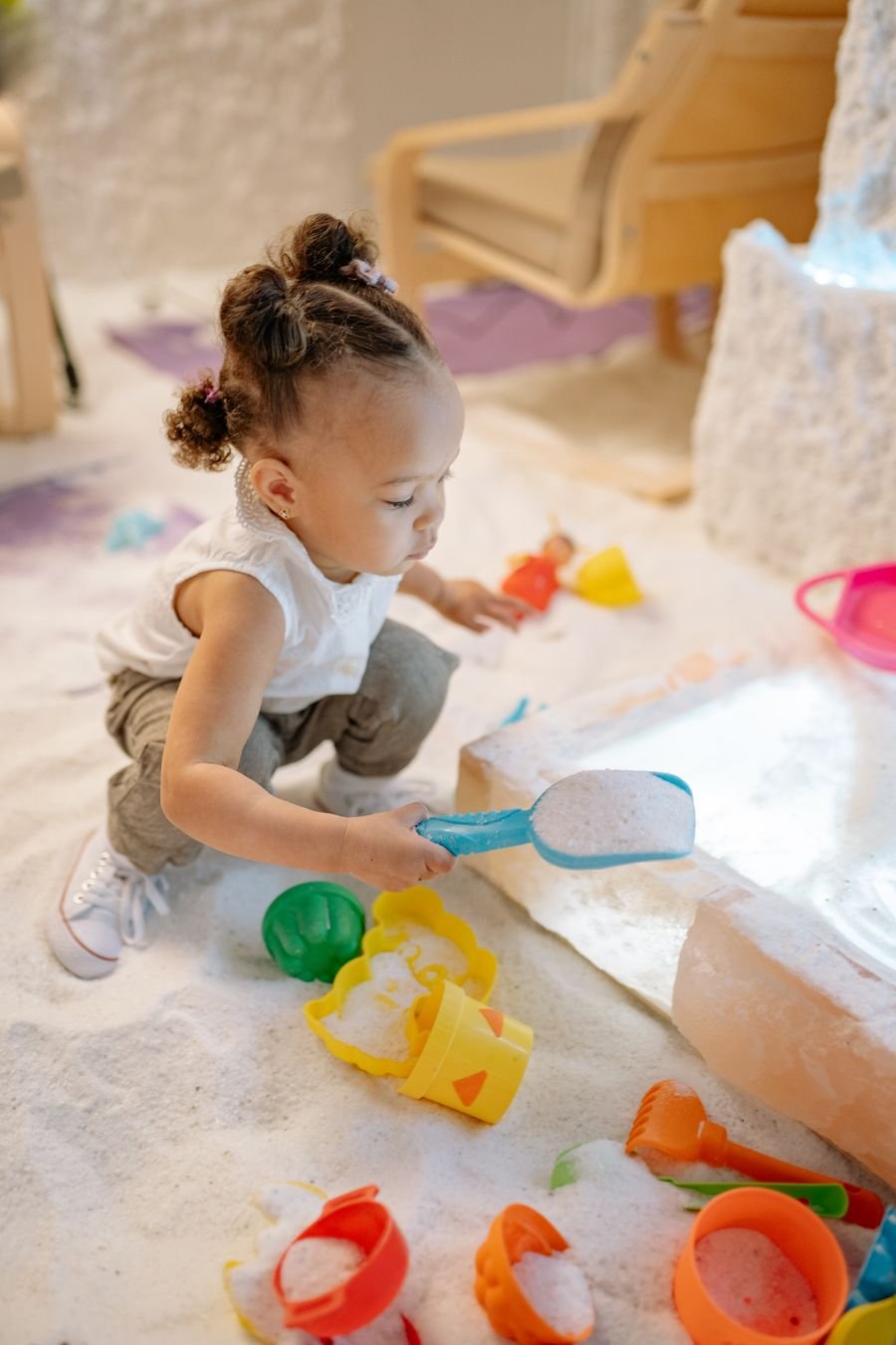 A young child kneeling at a sensory tray, scooping with a small spade